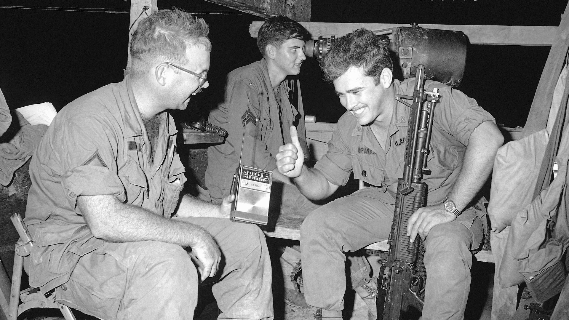 GIs on guard in bunker at Mekong delta base camp of U.S. Ninth division 25 miles southwest of Saigon, listen to radio broadcast of the Apollo ll launch on Wednesday, July 16, 1969. Spec. 4 Rodney D. Sparks of Wyandotte, Mich, gives thumbs-up sign as PFC Earl C. Hollingsworth III of Augusta, Ga. Grins at news of successful blast-off. In background Sgt. Stephen C. Dionne of Seattle views terrain outside bunker through a starlight scope. (AP Photo/Oliver Noonan)