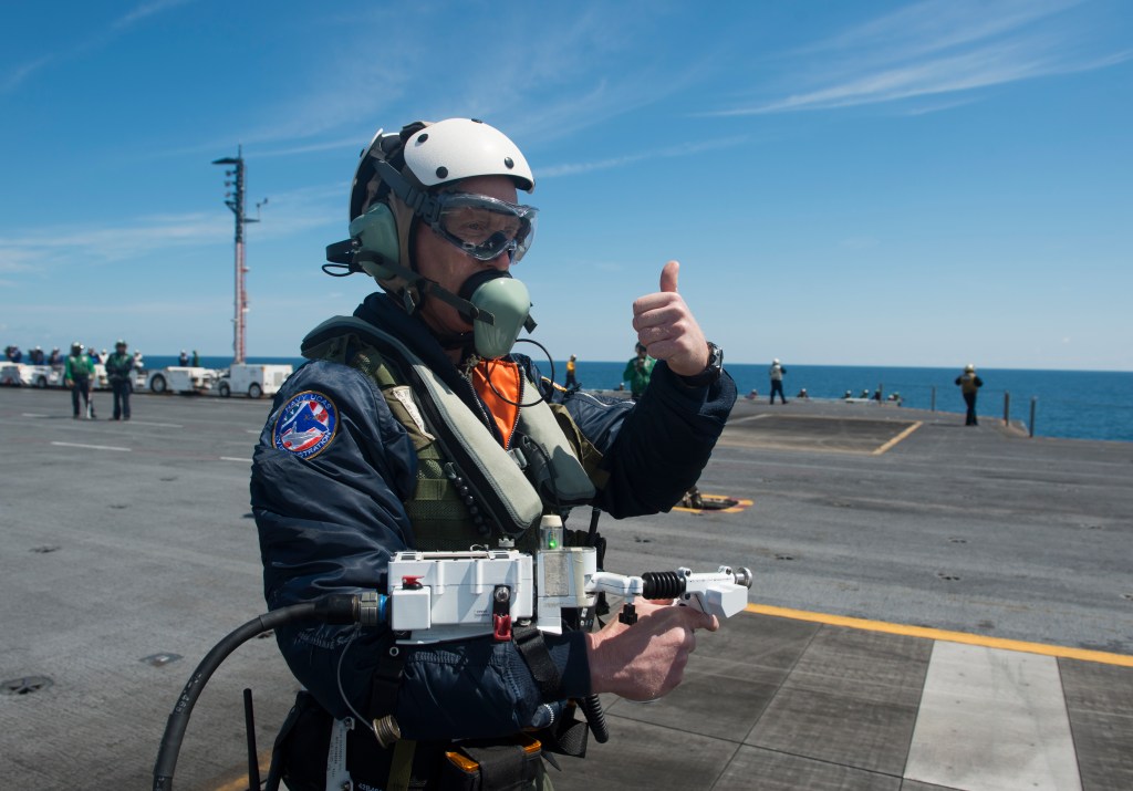 130514-N-FU443-673 ATLANTIC OCEAN (May 14, 2013) Dave Lorenz, a deck operator for Northrop Grumman, acknowledges that he has control of an X-47B Unmanned Combat Air System (UCAS) demonstrator as he moves it via an arm-mounted controller on the flight deck of the aircraft carrier USS George H.W. Bush (CVN 77). George H.W. Bush is scheduled to be the first aircraft carrier to catapult launch an unmanned aircraft from its flight deck. (U.S. Navy photo by Mass Communication Specialist 2nd Class Timothy Walter/Released)