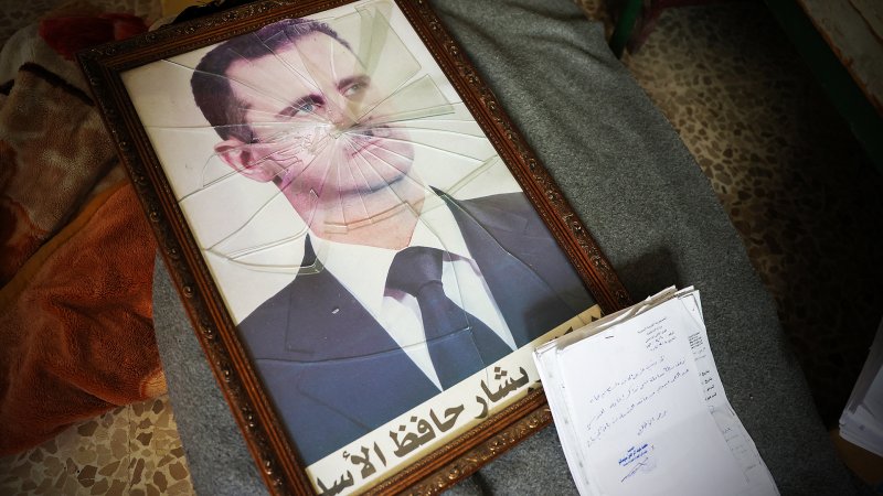 A portrait of Syrian President Bashar al-Assad is pictured with its frame broken, in a Syrian regime's Political Security Branch facility on the outskirts of the central city of Hama, following the capture of the area by anti-government forces, on December 7, 2024. Syria's embattled government said on December 7 it was setting up a ring of steel around Damascus, state media reported, as rebels on a lightning advance said they were bearing down on the city. The leader of Hayat Tahrir al-Sham (HTS), the Islamist group which has headed the assault, told fighters to prepare to take Damascus, just over a week into a renewed offensive in the long dormant conflict. (Photo by OMAR HAJ KADOUR / AFP) (Photo by OMAR HAJ KADOUR/AFP via Getty Images)