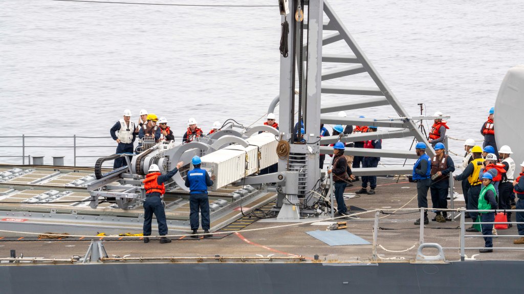 Sailors aboard Ticonderoga-class cruiser USS Chosin (CG 65) use the Transferrable Reload At-sea Method, or TRAM (gray machine at left), to grasp a missile canister (white, center) over the ship's forward MK 41 Vertical Launching System (VLS) during the first at-sea demonstration of TRAM off the coast of San Diego on Oct. 9. The canister traveled across cables from Military Sealift Command’s Lewis and Clark-class dry cargo and ammunition ship USNS Washington Chambers (T-AKE 11) to USS Chosin, where TRAM tilted it into a vertical position and lowered it into a VLS cell. (U.S. Navy photo by Eric Osborne)