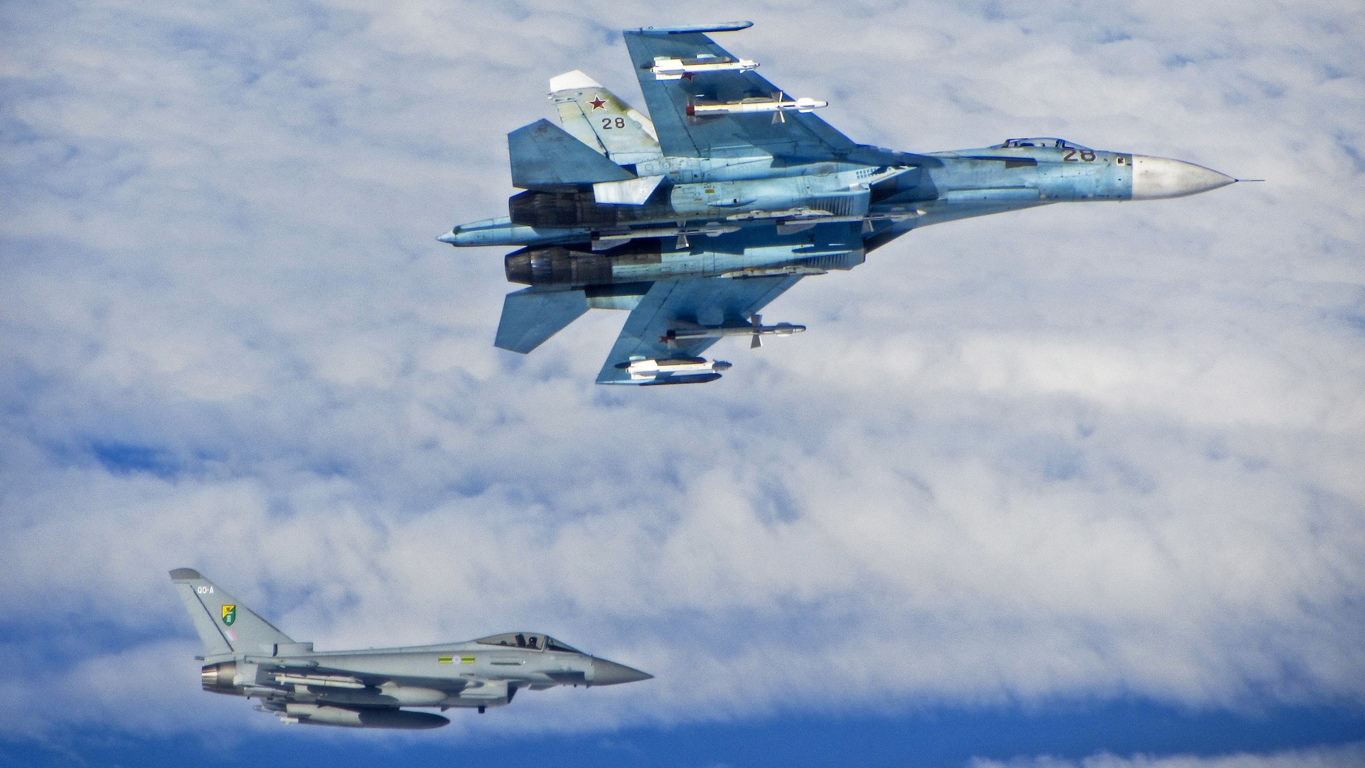 A Russian SU-27 Flanker aircraft banks away with a RAF Typhoon in the background. RAF Typhoons were scrambled on Tuesday 17 June 2014 to intercept multiple Russian aircraft as part of NATO’s ongoing mission to police Baltic airspace. The Typhoon aircraft, from 3 (Fighter) Squadron, were launched after four separate groups of aircraft were detected by NATO air defences in international airspace near to the Baltic States. Once airborne, the British jets identified the aircraft as a Russian Tupolev Tu22 ‘Backfire’ bomber, four Sukhoi Su27 ‘Flanker’ fighters, one Beriev A50 ‘Mainstay’ early warning aircraft and an Antonov An26 ‘Curl’ transport aircraft who appeared to be carrying out a variety of routine training. The Russian aircraft were monitored by the RAF Typhoons and escorted on their way. The Typhoon pilots involved in the operation were Flight Lieutenant (Flt Lt) Mark Long of 29 (Reserve) Squadron (the Typhoon operational training unit) and a French Air Force exchange pilot Commandant Marc-antoine Gerrard who is currently attached to 1(Fighter) Squadron.